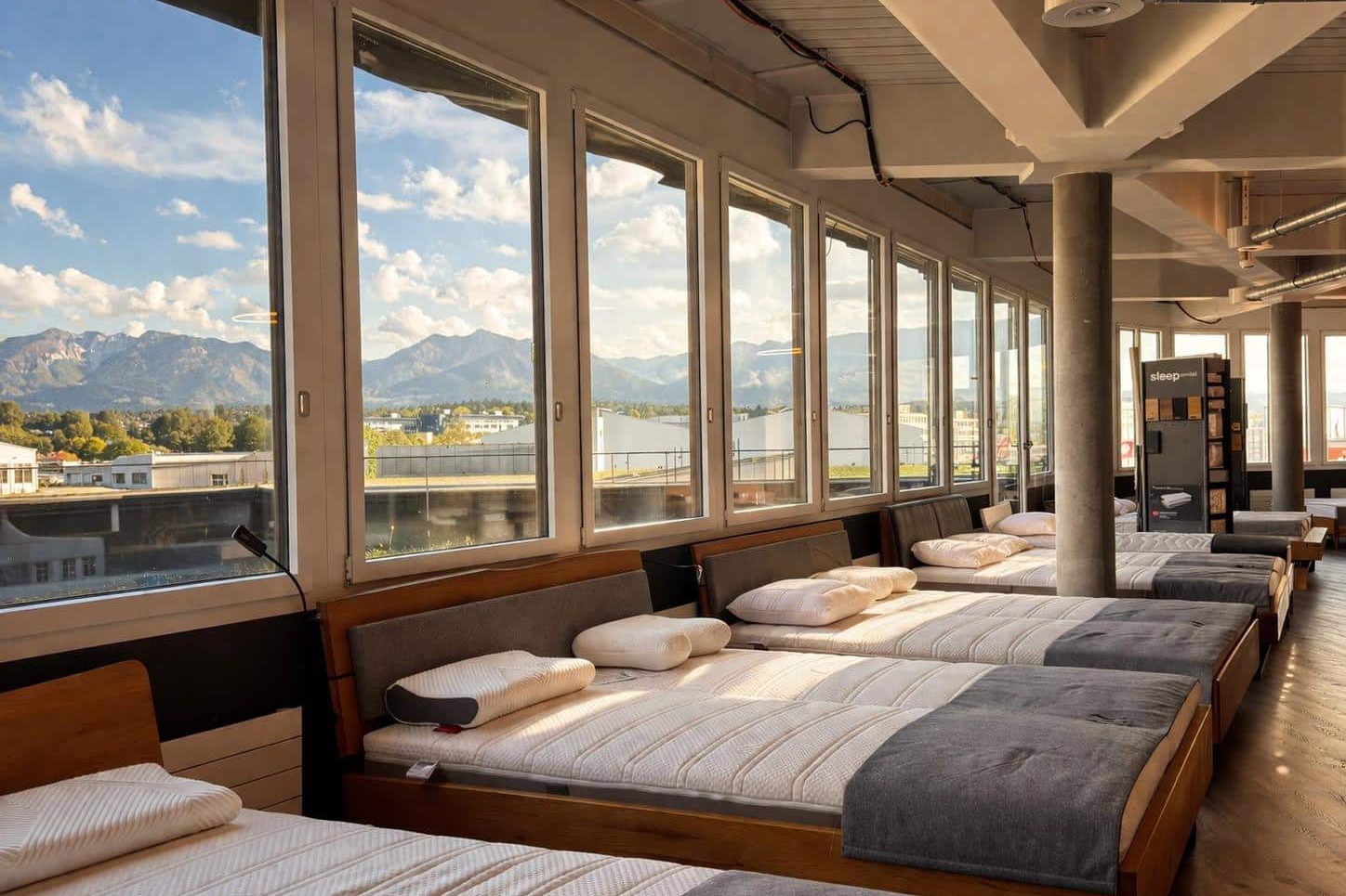 Des matelas à essayer près de la baie vitrée du showroom Mara Vital de Volketswil, avec vue sur les montagnes en arrière-plan.